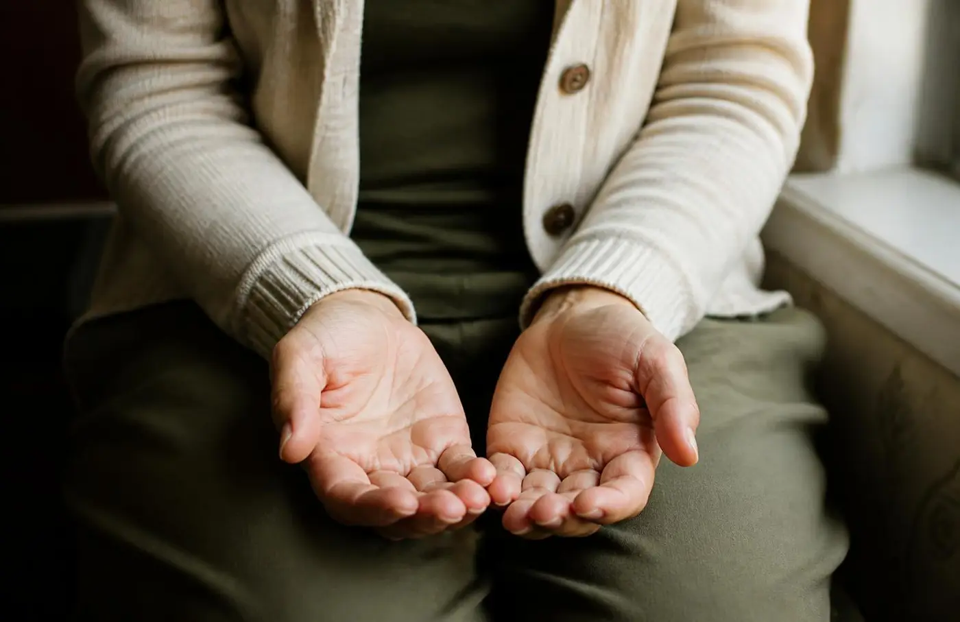 Open, upturned hands resting in a lap by a window in warm afternoon light